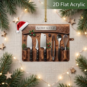 May include: A 2D flat acrylic ornament featuring a brown leather-look knife roll with the text CHEF ALEX. The design includes a Santa hat, kitchen tools like knives, a whisk, and tongs, decorated with holly berries and pine cones on a gold string.