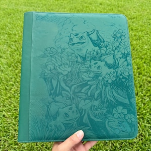 Può includere: Un raccoglitore verde acqua con un'illustrazione in rilievo di diversi personaggi Bulbasaur circondati da vari fiori e fogliame. La copertina ha una superficie testurizzata e un pannello verticale sul dorso sinistro con una finitura liscia.