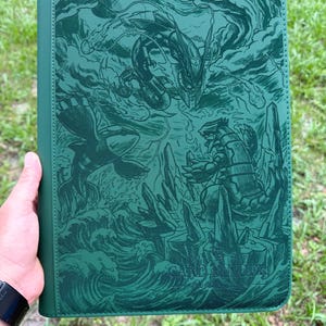 Puede incluir: Una carpeta rectangular de color verde oscuro con una intrincada ilustración en relieve de tres criaturas legendarias. El diseño muestra un dragón serpentino, una criatura marina sobre olas oceánicas y una bestia rocosa entre formaciones de piedra.