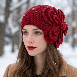 May include: A deep red crochet beanie featuring a large, multi-layered, dimensional flower accent on the side. The hat is constructed with a dense, textured stitch pattern and covers the crown of the head, providing a snug fit with a prominent floral detail.