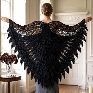 Può includere: Uno scialle all'uncinetto nero con un design a uccello con ali spiegate e dettagliate texture simili a piume. Il capo presenta un motivo a rete aperta sulla parte superiore della schiena e sulle spalle, estendendosi in un'ampia silhouette alata.