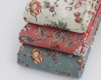 May include: Three pieces of fabric with floral patterns. The top fabric is cream with pink and green flowers. The middle fabric is coral with pink and green flowers. The bottom fabric is blue with pink and green flowers.