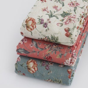 Puede incluir: Tres piezas de tela con estampados florales. La tela superior es crema con flores rosas y verdes. La tela del medio es coral con flores rosas y verdes. La tela inferior es azul con flores rosas y verdes.