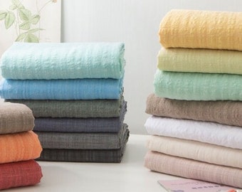 May include: A stack of ten fabric swatches in various colors, including light blue, gray, white, beige, orange, and red. The swatches are folded and arranged on a white table.