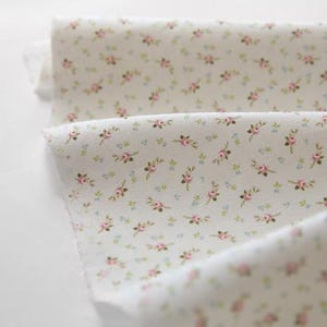 May include: Close-up of a folded fabric with a delicate floral pattern. The fabric is white with small pink and green floral sprigs scattered across the surface. The fabric is soft and appears to be cotton.