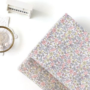 May include: A white fabric with a small floral pattern in pink, yellow, and blue. The fabric is folded in half and is lying on a white surface.