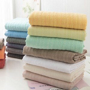 May include: A stack of ten fabric swatches in various colors, including light blue, yellow, green, brown, white, and pink. The swatches are folded and stacked on a white surface.
