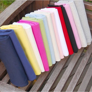 May include: A collection of fabric swatches in various colors, including navy blue, yellow, white, pink, green, light blue, beige, and red. The fabric swatches are folded and arranged in a row on a wooden surface.