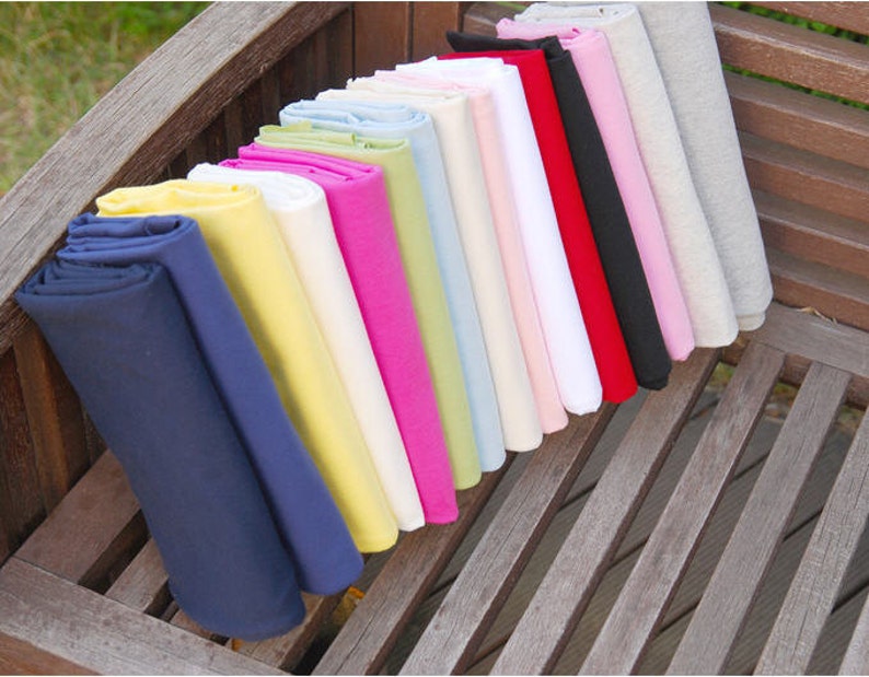 May include: A collection of fabric swatches in various colors, including navy blue, yellow, white, pink, green, light blue, beige, and red. The fabric swatches are folded and arranged in a row on a wooden surface.