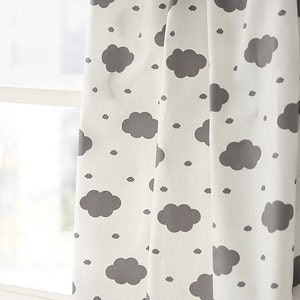 May include: White curtain with a repeating pattern of gray clouds. The clouds vary in size, with larger, fluffy shapes and smaller, dot-like clouds. The curtain is hanging in front of a window, with natural light illuminating the fabric.