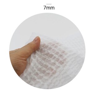 May include: Close-up of a white, textured fabric with a grid pattern. The fabric is 7mm thick.