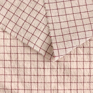 May include: Two pieces of beige fabric with a red checkered pattern. The fabric is folded over itself, showing the pattern on both sides.