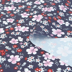 Op de afbeelding: Een donkerblauwe stof met een roze en witte bloemenprint. De stof is dubbelgevouwen om de lichtblauwe onderkant te laten zien.