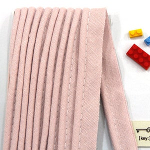 May include: A close-up of a pink fabric trim with a stitched edge. The trim is folded and stacked, showing the texture of the fabric.