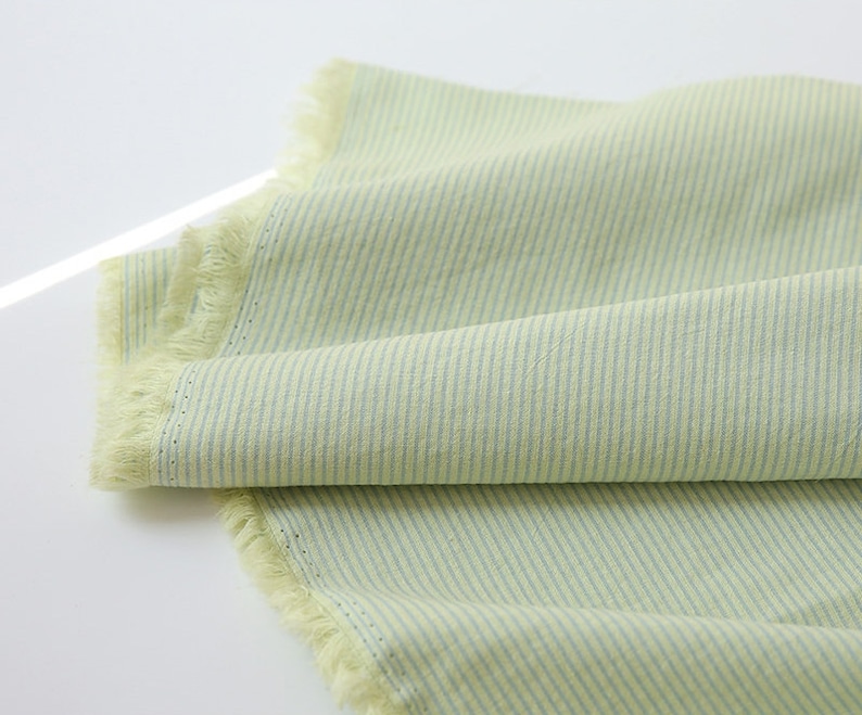 May include: A light green fabric with thin white stripes. The fabric has a frayed edge.