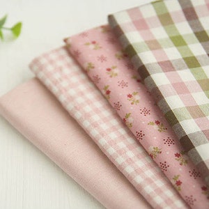 May include: Four pieces of fabric stacked on top of each other. The top fabric is a brown and pink plaid, the second fabric is a pink floral print, the third fabric is a pink and white gingham, and the bottom fabric is a solid pink.
