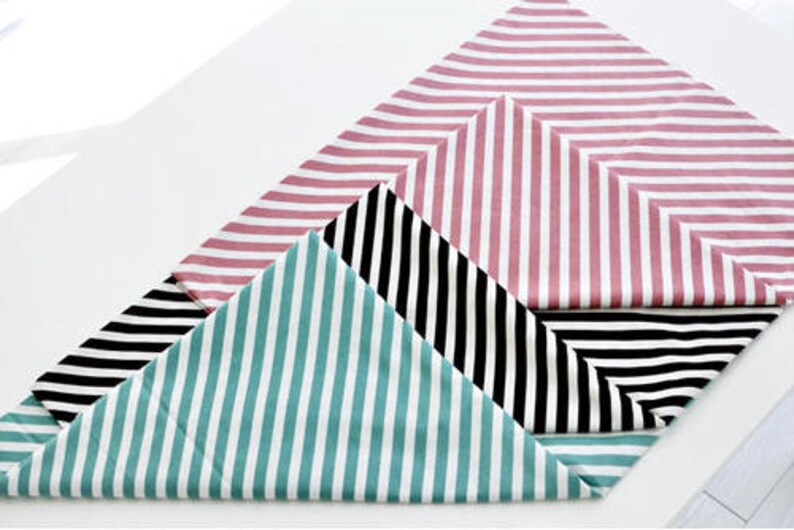 Puede incluir: Tres caminos de mesa de tela a rayas en rosa, negro y blanco, y azul verdoso. Los caminos de mesa est&aacute;n doblados en forma triangular.