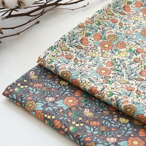May include: Two pieces of fabric with a floral pattern. The fabric on top is cream with orange, yellow, and blue flowers. The fabric on the bottom is gray with orange, yellow, and blue flowers.