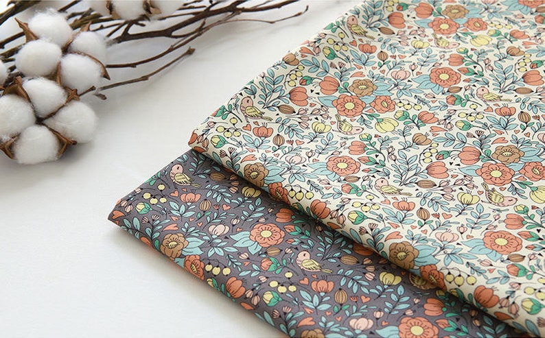 May include: Two pieces of fabric with a floral pattern. The fabric on top is cream with orange, yellow, and blue flowers. The fabric on the bottom is gray with orange, yellow, and blue flowers.
