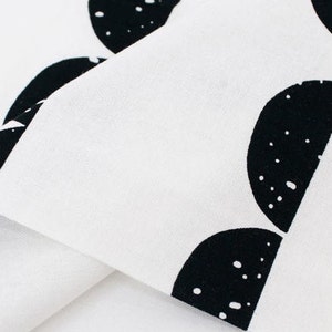 May include: White fabric with a black and white pattern of half circles. The fabric is folded over itself, showing the white side of the fabric.
