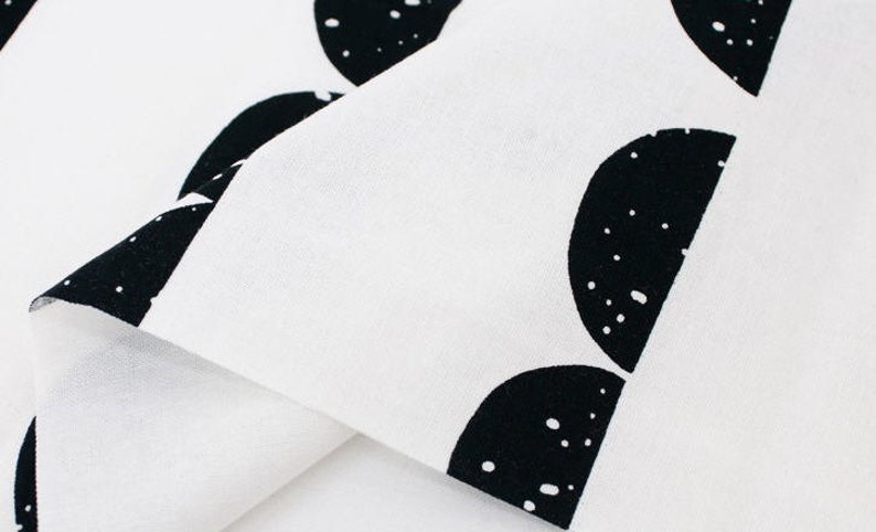 May include: White fabric with a black and white pattern of half circles. The fabric is folded over itself, showing the white side of the fabric.
