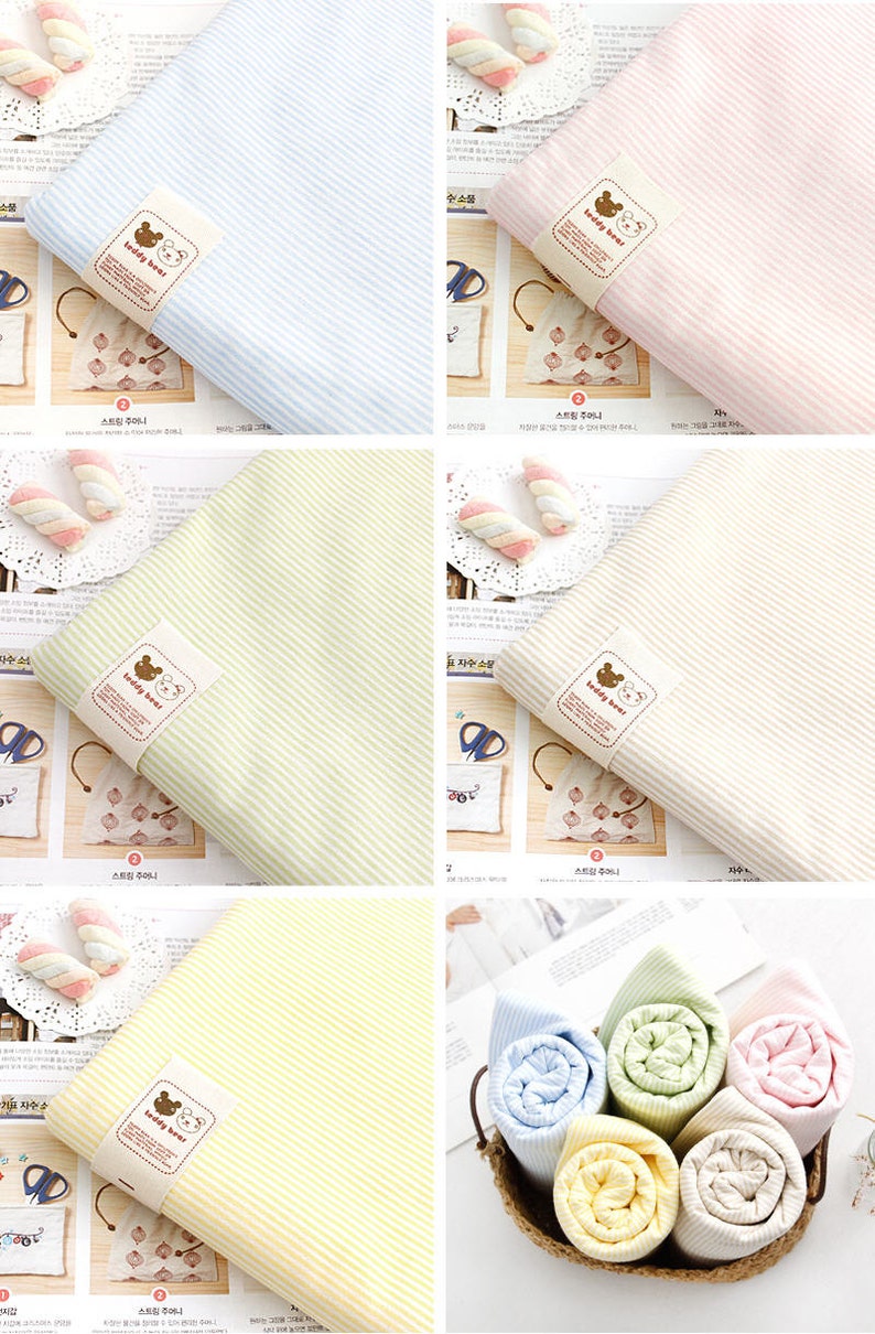 May include: Four different striped fabric swatches with a teddy bear logo. The fabric swatches are in blue, pink, green, and yellow. The swatches are rolled up in a basket.