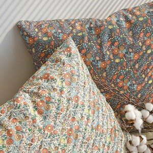 May include: Two decorative throw pillows with floral patterns. The pillow on top has a light background with orange, yellow, and blue flowers. The bottom pillow has a dark background with orange, yellow, and blue flowers.