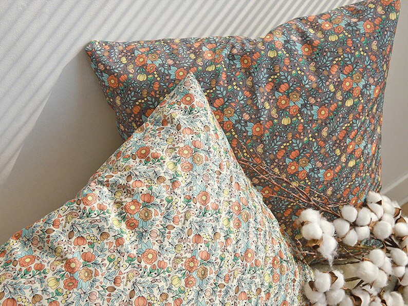 May include: Two decorative throw pillows with floral patterns. The pillow on top has a light background with orange, yellow, and blue flowers. The bottom pillow has a dark background with orange, yellow, and blue flowers.