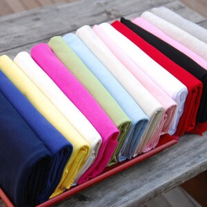 May include: A collection of folded fabric swatches in various colors, including navy blue, yellow, white, pink, light green, light blue, and red. The swatches are arranged in a row on a wooden surface.