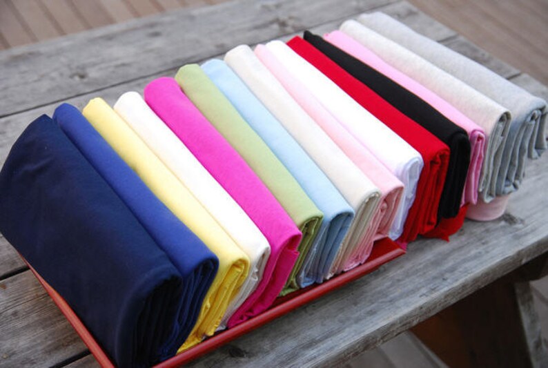 May include: A collection of folded fabric swatches in various colors, including navy blue, yellow, white, pink, light green, light blue, and red. The swatches are arranged in a row on a wooden surface.