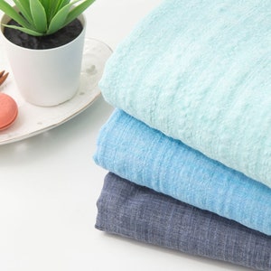 May include: Stack of three fabric swatches in shades of blue. The top swatch is a light blue, the middle swatch is a medium blue, and the bottom swatch is a dark blue. The swatches are folded and arranged on a white surface.