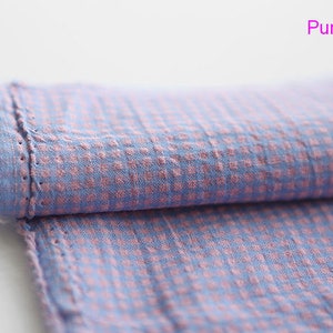 Pu&ograve; includere: Un pezzo di stoffa piegato con un motivo a quadri in tonalit&agrave; rosa e blu. Il tessuto ha una superficie leggermente strutturata e un bordo grezzo.