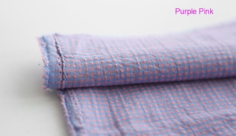 Pu&ograve; includere: Un pezzo di stoffa piegato con un motivo a quadri in tonalit&agrave; rosa e blu. Il tessuto ha una superficie leggermente strutturata e un bordo grezzo.