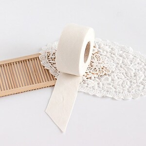 May include: A roll of off-white tape with a textured surface, partially unrolled, resting on a white lace doily and a small bamboo tray. The tape appears to be made of a soft, fibrous material.