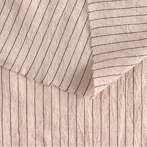 May include: Close-up of a cream-colored fabric with thin, red stripes. The fabric has a textured, slightly rough surface.