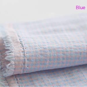 Pu&ograve; includere: Un primo piano di un tessuto gingham blu e rosa con un bordo sfrangiato. Il tessuto &egrave; piegato a met&agrave; e sono visibili i quadrati blu e rosa.