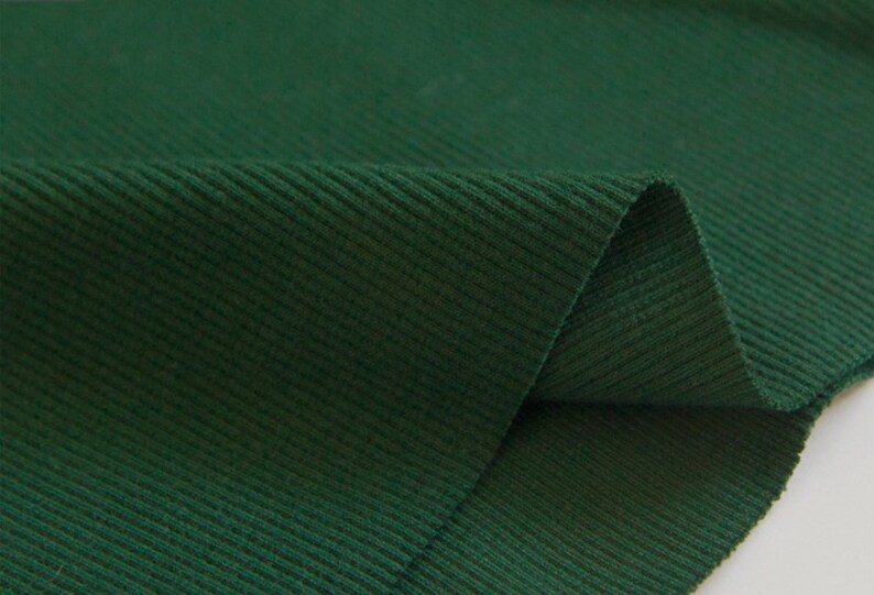 May include: Close-up of a dark green ribbed fabric. The fabric has a soft, textured surface.