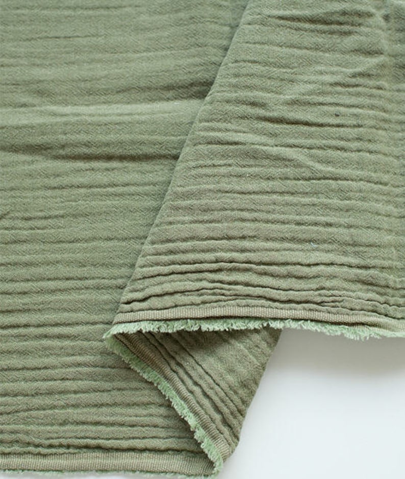 May include: A close-up of a folded piece of green fabric with a textured surface. The fabric has a raw edge and is folded over itself.