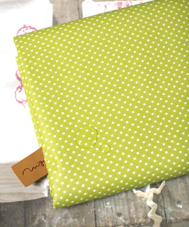 May include: A green fabric with white polka dots. The fabric is waterproof and has water droplets on it.