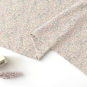 May include: A close-up of a white fabric with a delicate floral pattern in shades of pink, yellow, and grey. The fabric is folded in half, revealing the pattern on both sides.