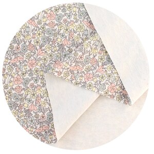 May include: A close-up of a white fabric with a floral pattern in shades of pink, yellow, and blue. The fabric is folded in half, revealing a plain white side.