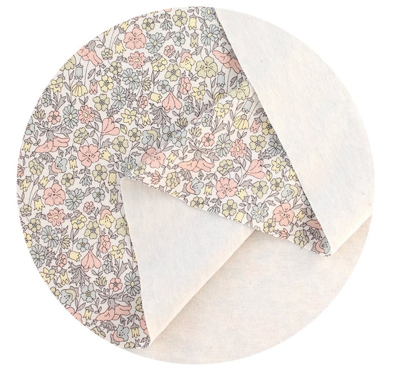 May include: A close-up of a white fabric with a floral pattern in shades of pink, yellow, and blue. The fabric is folded in half, revealing a plain white side.