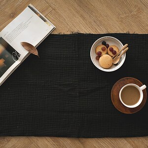 Op de afbeelding: Een zwarte stoffen placemat met een kop koffie, een bord met koekjes en druiven en een boek met een zonsondergangfoto op de omslag.