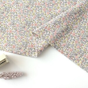 May include: White fabric with a small pink and yellow floral print. The fabric is folded in half and the edges are visible.