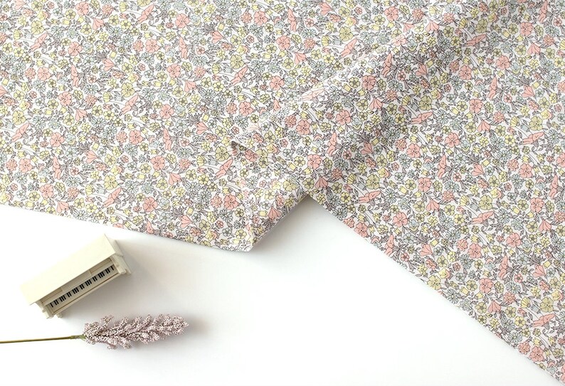 May include: White fabric with a small pink and yellow floral print. The fabric is folded in half and the edges are visible.