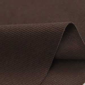 May include: Close-up of a brown corduroy fabric with a subtle ribbed texture. The fabric is folded in half, showing the soft, plush surface.