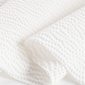 May include: Close-up of a white, textured fabric with a waffle-weave pattern. The fabric is folded, revealing layers and shadows. The material appears soft and lightweight, suitable for various textile applications.