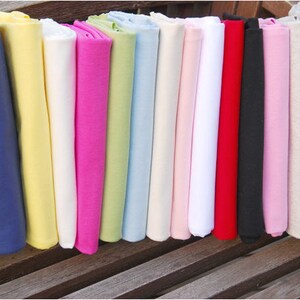 May include: A collection of 15 fabric swatches in various colors, including navy blue, yellow, white, pink, green, light blue, red, black, and gray. The swatches are folded and arranged in a row on a wooden surface.