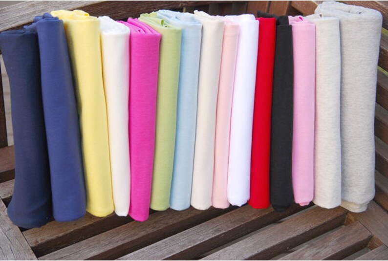 May include: A collection of 15 fabric swatches in various colors, including navy blue, yellow, white, pink, green, light blue, red, black, and gray. The swatches are folded and arranged in a row on a wooden surface.