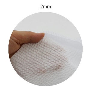 May include: Close-up of a white, textured, paper towel. The towel is being held by a hand and is folded in half. The text "2mm" is visible above the towel.